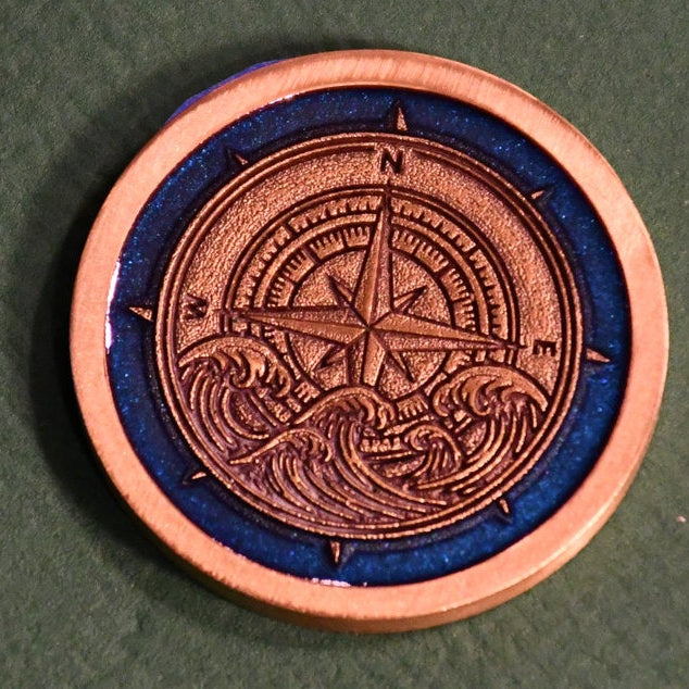 A circular copper-colored medallion featuring an embossed compass and wave design, set against a dark textured background.